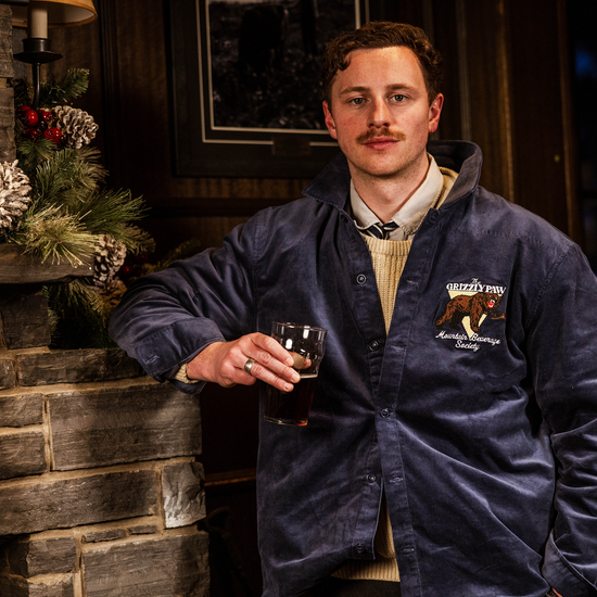 Man in a blue jacket holding a glass in a cozy indoor setting with a stone wall and festive decorations.