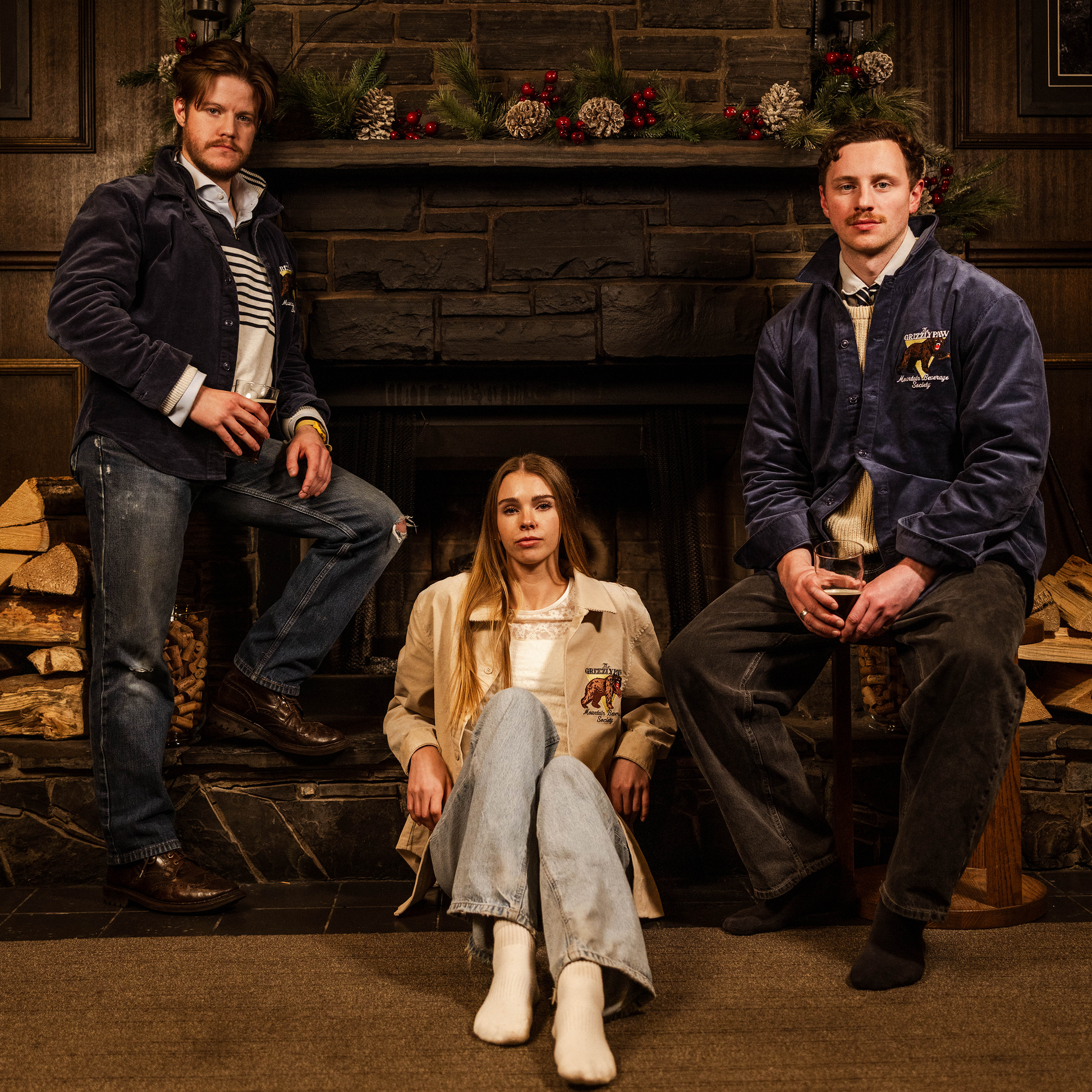 Three people sitting in front of a fireplace with decorative items on the mantel.