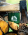 A dark green enamel camping mug with a white graphic of a bear and pine trees, resting on a pile of firewood with an axe in the background.